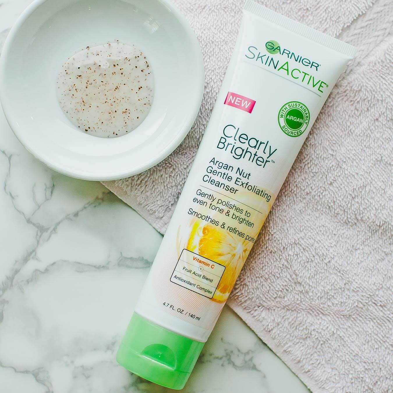 Garnier SkinActive Clearly Brighter Argan Nut Gentle Exfoliating Cleanser on a tan towel and white bowl holding a small amount of product on white marble.